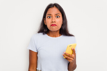 Young indian woman using mobile phone isolated on white background shrugs shoulders and open eyes confused.