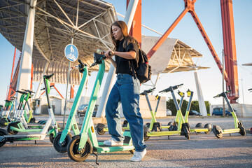 Teen woman standing at the powered scooter and unlocking it by smartphone