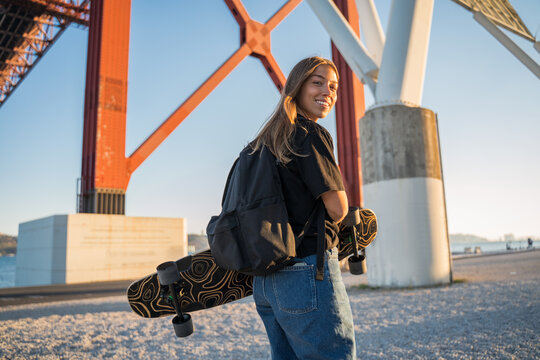 Woman carrying skateboard while walking through the embankment near the sea