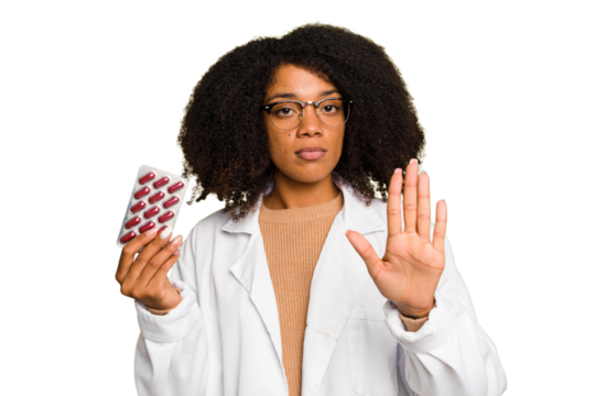Young pharmacist African American woman holding a tablet of pills isolated standing with outstretched hand showing stop sign, preventing you.