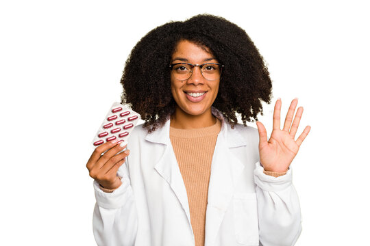 Young pharmacist African American woman holding a tablet of pills isolated smiling cheerful showing number five with fingers.