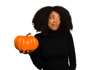 Young African American woman holding a pumpkin for halloween day isolated confused, feels doubtful and unsure.