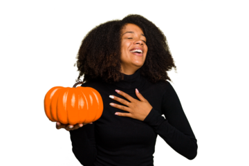 Young African American woman holding a pumpkin for halloween day isolated laughs out loudly keeping hand on chest.