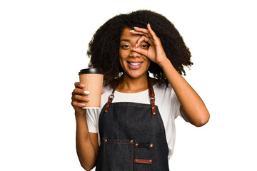 Young african american woman barista holding a takeaway coffee excited keeping ok gesture on eye.