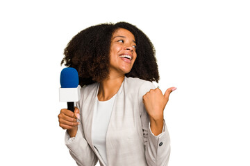Young TV presenter African American woman with a microphone isolated points with thumb finger away, laughing and carefree. - obrazy, fototapety, plakaty
