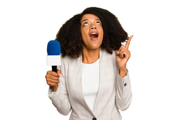 Young TV presenter African American woman with a microphone isolated pointing upside with opened mouth. - obrazy, fototapety, plakaty