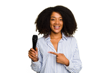 Young African American singer woman holding a microphone isolated smiling and pointing aside, showing something at blank space.