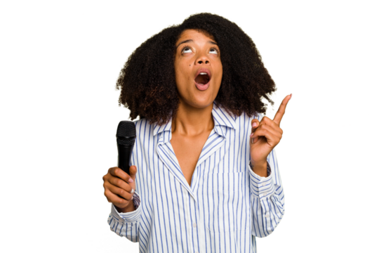 Young African American singer woman holding a microphone isolated pointing upside with opened mouth.