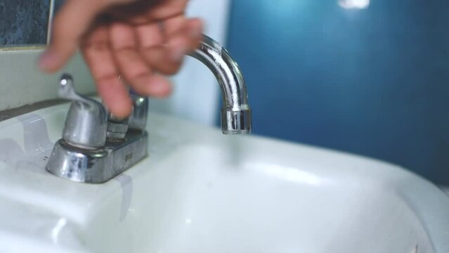 Mano de un joven hombre abre la llave del agua caliente del grifo del ba&ntilde;o para que caiga el agua 