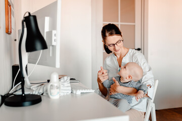 Mother working on computer with baby in hands. Working mother with kid.