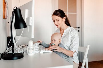 Mother working on computer with baby in hands. Working mother with kid.