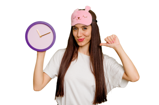 Young caucasian woman wearing pajama and holding a clock feels proud and self confident, example to follow.