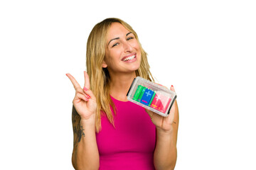 Young caucasian woman holding battery box isolated on green chroma background joyful and carefree...