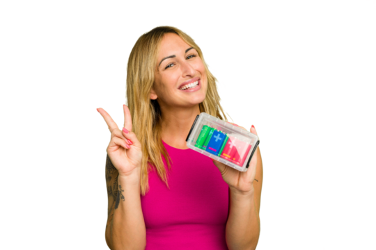 Young caucasian woman holding battery box isolated on green chroma background joyful and carefree showing a peace symbol with fingers. - Powered by Adobe