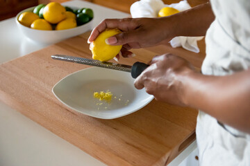 Black woman, African American woman hands zesting a lemon with fine grater on a wooden cutting board