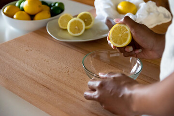 African American woman hands holding half cut lemon cross section above glass bowl. Copy Space
