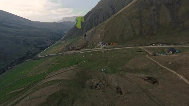 Aerial view man paraglider flying extreme sport activity at mountain rocky terrain valley enjoy freedom. FPV drone shot paraplane parachute outdoor adventure over cliff summit sky countryside scenery