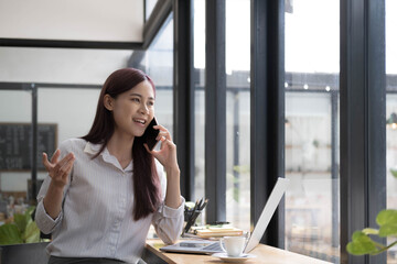 Smiling beautiful Asian businesswoman analyzing chart and graph showing changes on the market and holding smartphone at office.