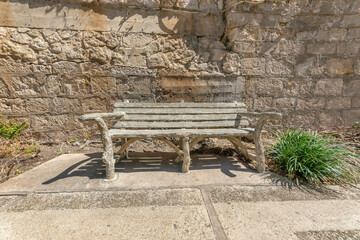Outdoor wooden bench against rough stone wall viewed on a sunny day