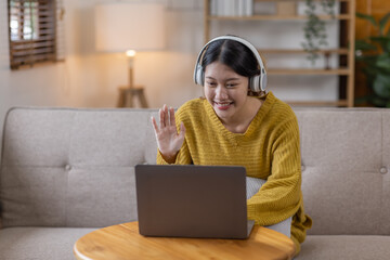 Beautiful Asian woman in white headphones and laptop sits on a sofa and enjoys listening to music, podcast, Enjoying Free Time Leisure On Sofa Everyday Life Concept. 