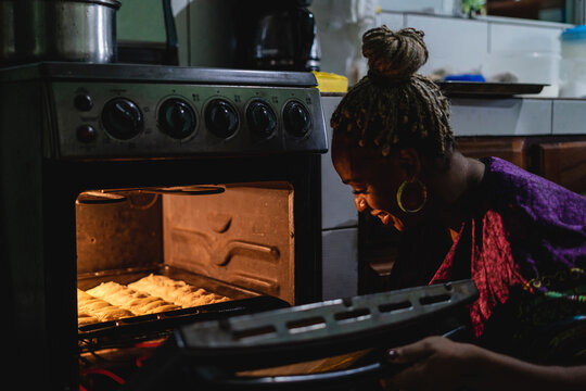 Imagen horizontal de una mujer afrocaribe&ntilde;a en el interior de su cocina sacando del horno unos bocadillos caribe&ntilde;os que acaba de preparar. 