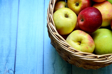 Fresh ripe apples in the basket on blue wooden background. Autumn harvest, organic fruits or gardening concept. Selective focus.