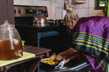 Mujer afrocaribeña en el interior de su cocina sacando del horno unos bocadillos caribeños que...