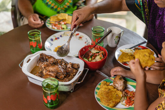 Imagen horizontal de una familia afrocaribe&ntilde;a irreconocible degustando un delicioso  almuerzo caribe&ntilde;o. 
