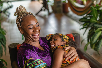 Imagen horizontal de una madre y su hija afrocaribeñas muy alegres y sonrientes jugando juntas en...