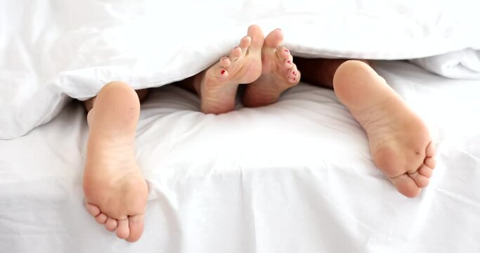 Male and female feet lying under covers in bed closeup 4k movie slow motion