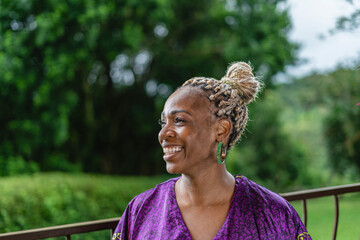 Retrato horizontal de una hermosa mujer afrocaribeña muy sonriente en el exterior de su casa  con un vestido caribeño muy colorido disfrutando de un día de verano.