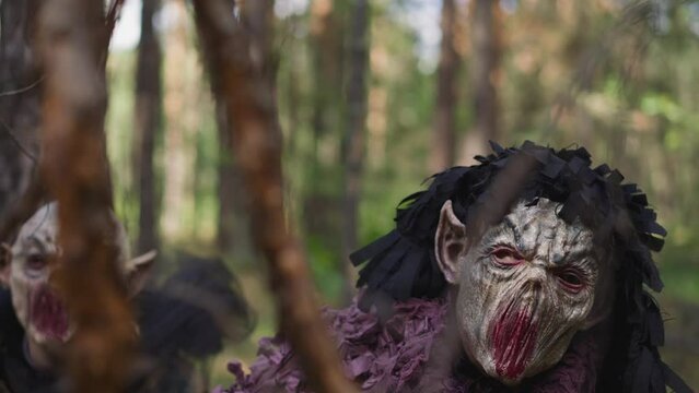 Scary demons look for lost travelers in forest closeup slow motion. Evil goblins wait for bag hiding in wood. Horror film set and actors