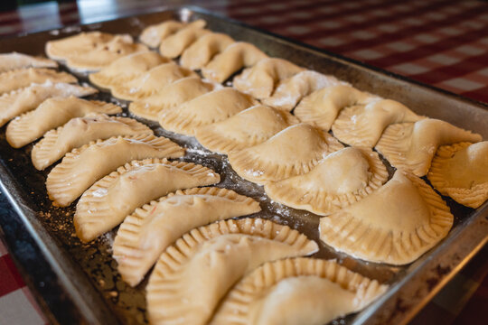 Imagen horizontal de unas deliciosas empanadas crudas al estilo caribe&ntilde;o en una bandeja sobre una mesa en el interior de una casa listas para ser horneadas.