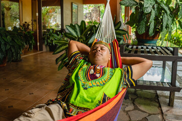 Imagen horizontal de un hombre latino adulto acostado en una hamaca de tela en su casa descansando. 