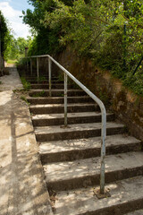 escalier extérieur en béton, avec une rampe métallique et une pente douce pour les cycles et les trotinettes ou les poussettes d'enfants; Verdure, arbres et buissons sauvages