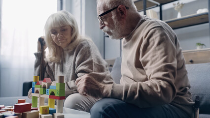 retired couple with dementia playing with colorful building blocks on table.