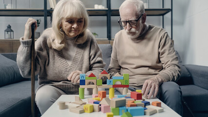Senior couple with dementia playing with colorful building blocks on table.