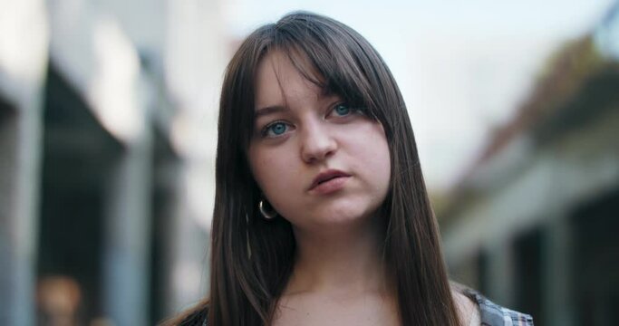 A close-up of the face of a young girl standing on the estate and watching the events, a team of friends. The teenager is chewing gum and turning her head from side to side.