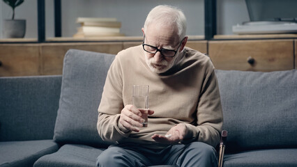 Senior man with dementia holding pills and glass of water at home.