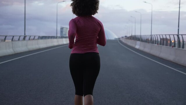 4k Woman athlete runs and works out on bridge in city spbas. Close view of young female runner is running with effort and doing cardio activity, posing outdoors. Curly athletic person does fitness and