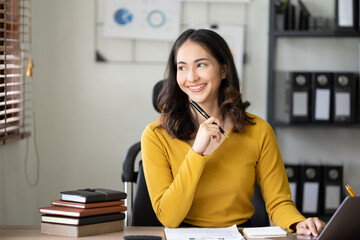 Happy businesswoman typing on laptop at her desk looking at camera in bright office