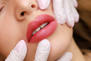 Chic lips of a young model on which permanent lip makeup is performed, the master stretches the...