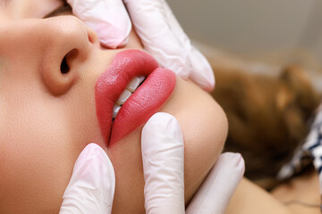 close-up of sexy lips of young models on which permanent lip makeup is performed, the master stretches the tips of the model's lips with his fingers - obrazy, fototapety, plakaty