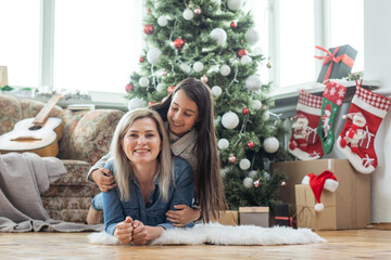 Merry Christmas and Happy Holidays. Cheerful mother and her cute daughter girl exchanging gifts. Mom and little child having fun near tree indoors. Loving family with presents in room