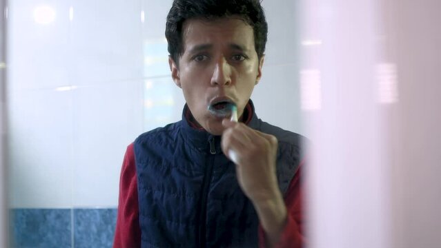 Joven hombre caucasico lavandose los dientes en el espejo de un ba&ntilde;o 