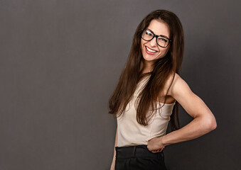 Beautiful confident thinking toothy smiling business brunette woman in glasses with folded arms in white shirt on grey background with empty copy space for text. Closeup