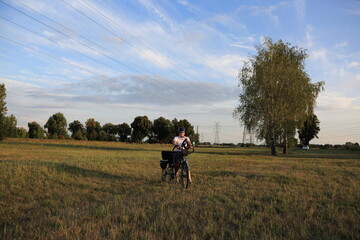 Mężczyzna z rowerem turystyczny na łące, w tle brzozy.	