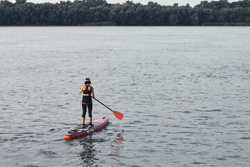 Back view of woman rowing on stand up paddle board (SUP) on river