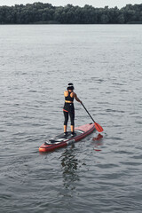 Back view of woman rowing on stand up paddle board (SUP) on river. Vertical photo