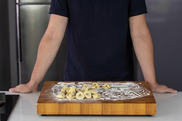 Chef cook hands making handmade Tortellini ravioli on wooden cut board with flour. Italian cuisine.